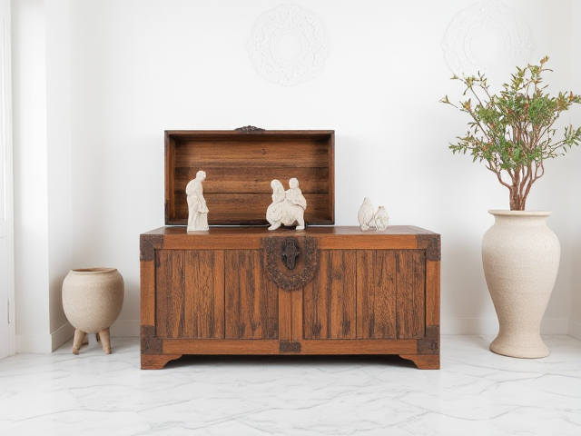 Je veux une image d'un coffre ancien en bois foncé avec des scultures dans une pièce entièrement blanche avec sol en marbre et moulure au mur