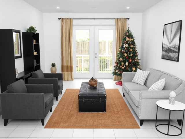 a small enclosed step down living room, absolutely no windows, just white walls on both sides, only one white double french door facing me with space on both sides of the door, french doors lead to backyard, white tiles, 3 sitting furniture (2 charcoal grey furniture, and 1 really high back light gray love seat with rhinestones that seats two persons), tan area rug and 3x5ft black bookshelf flush against the left wall in the corner, absolutely no furniture in front of the french doors or bookshelf, two white round end tables with black metal legs,  just ONE big black and gold christmas tree and gold and white ombre curtains on the french doors, black trunk in the center of the rug, also add any other aesthetic to enhance the room