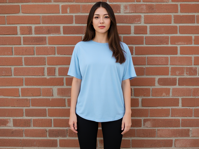 finite brunettes hair down wearing a light blue loose t shirt that cuts at her knees and black yoga pants lined up against a brick wall